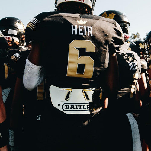 a group of football players standing next to each other and one has a white and black Battle back plate with the word battle on it written in black